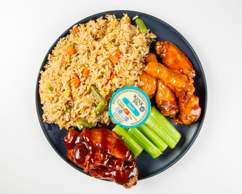A plate of fried rice, barbecue wings, buffalo wings, celery sticks, and a ranch dressing cup.