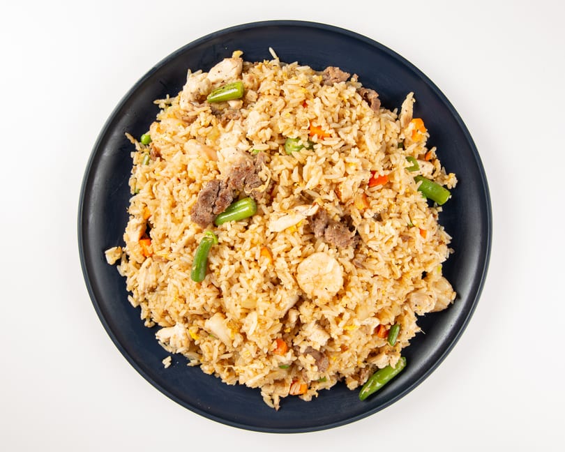 A dark plate filled with fried rice, chicken, beef, shrimp, green beans, and carrots.