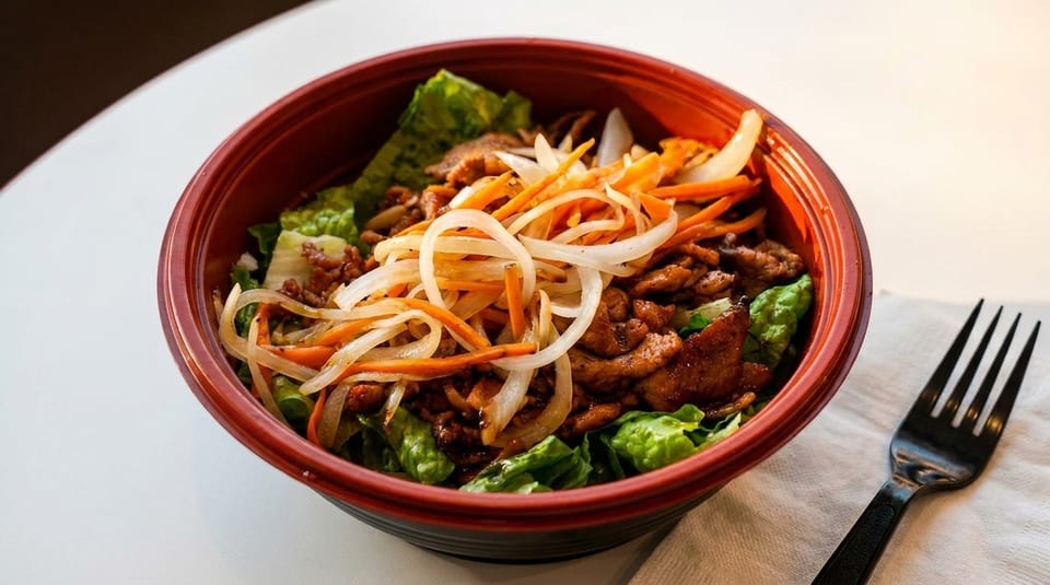 A vibrant bowl of Korean bulgogi with lettuce, shredded carrots, and onions, next to a black fork.