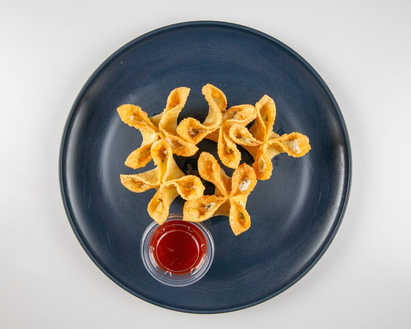 Crispy crab rangoons with sweet and sour sauce on a dark blue plate.
