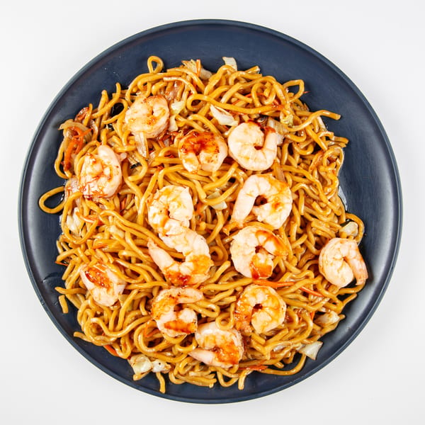 Shrimp lo mein with noodles, cabbage, and carrots on a dark blue plate.