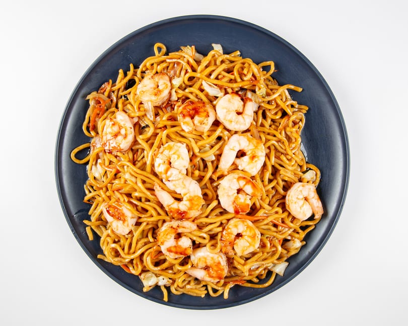 Shrimp lo mein with noodles, cabbage, and carrots on a dark blue plate.