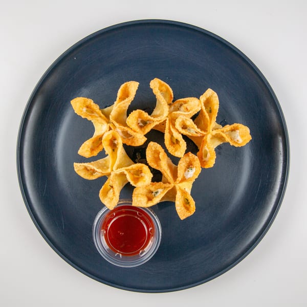 Crispy crab rangoons with sweet and sour dipping sauce on a dark blue plate.