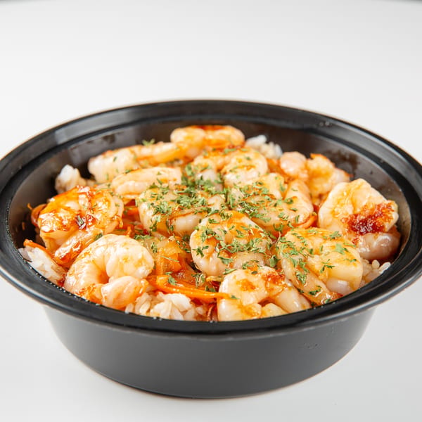 Shrimp and rice bowl with vegetables and parsley in a black container.