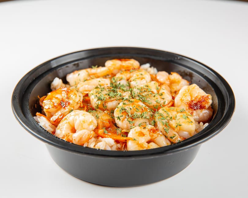 Shrimp and rice bowl with vegetables and parsley in a black container.
